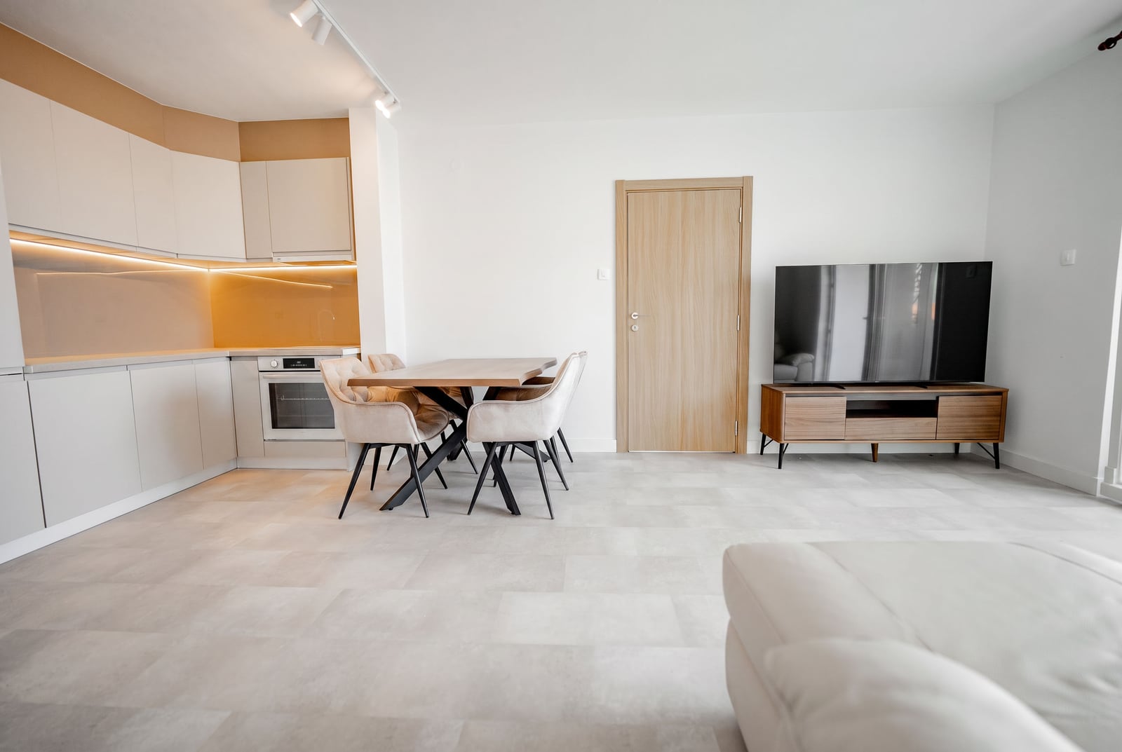 Modern living room with kitchen in an apartment, Sveti Stefan, Montenegro: light furniture, dining area, and TV stand.