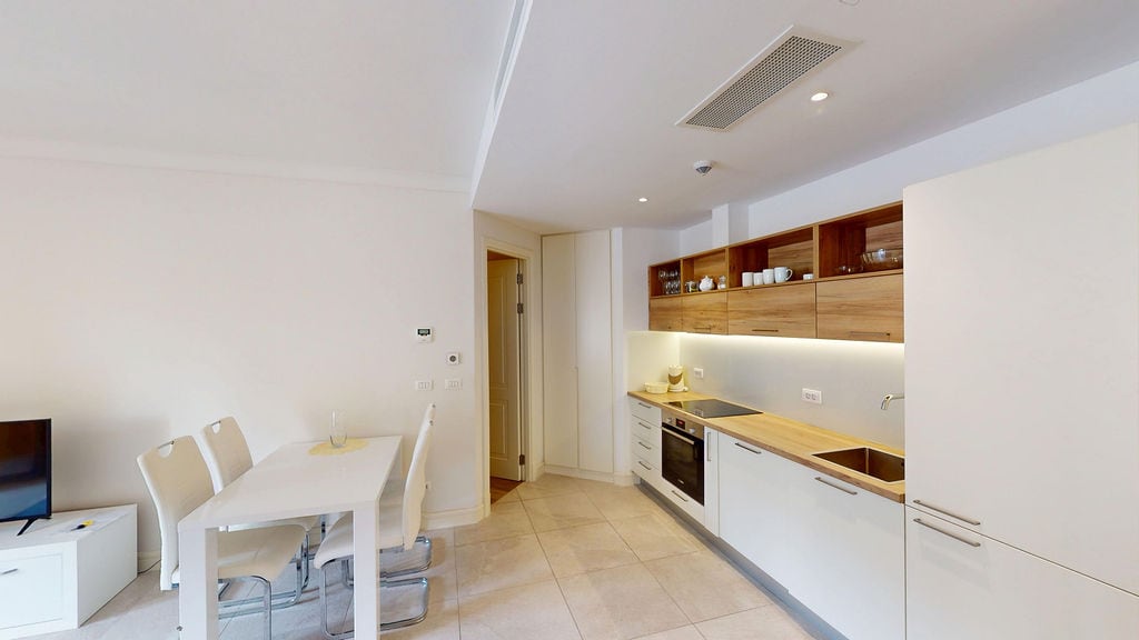 Modern kitchen-dining room in an apartment, Luštica, Montenegro: white furniture, built-in appliances, and a dining area.