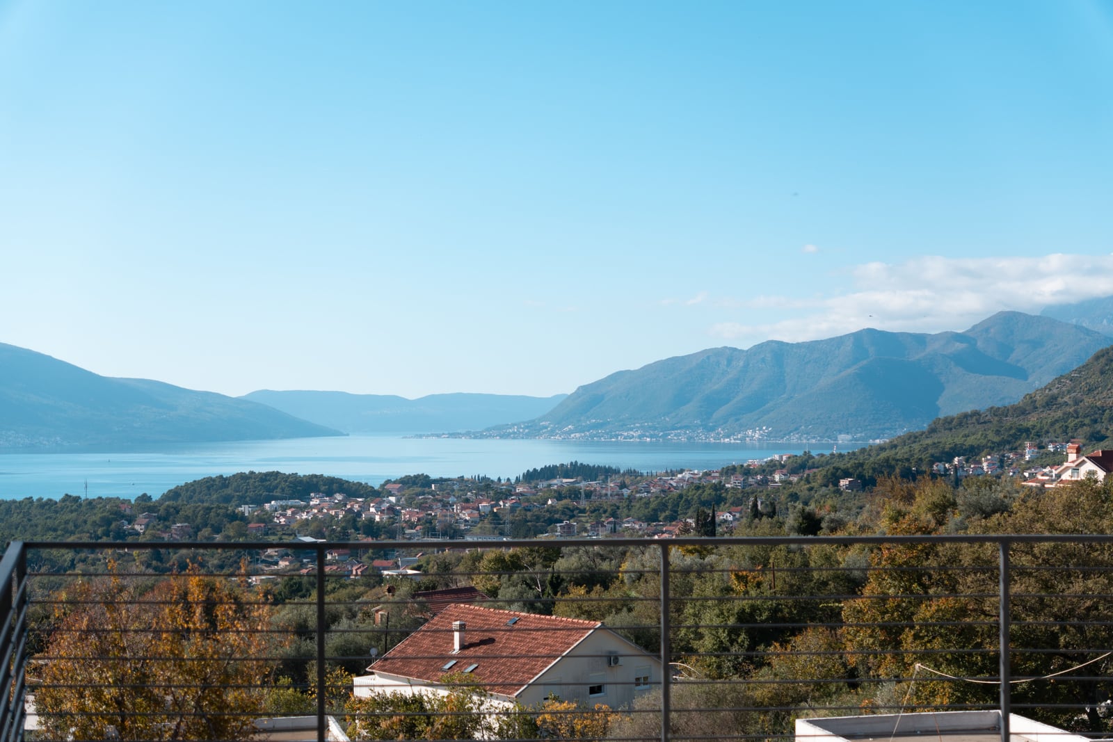 Panoramic view of the Bay of Kotor from a townhouse balcony in Kavač, Montenegro: mountains, sea, and private residential area.