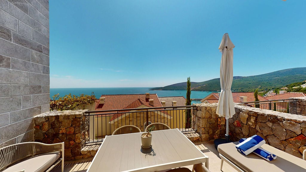 Furnished terrace with sea view at Luštica residential complex, Montenegro: stone finish, table, and lounge chair.