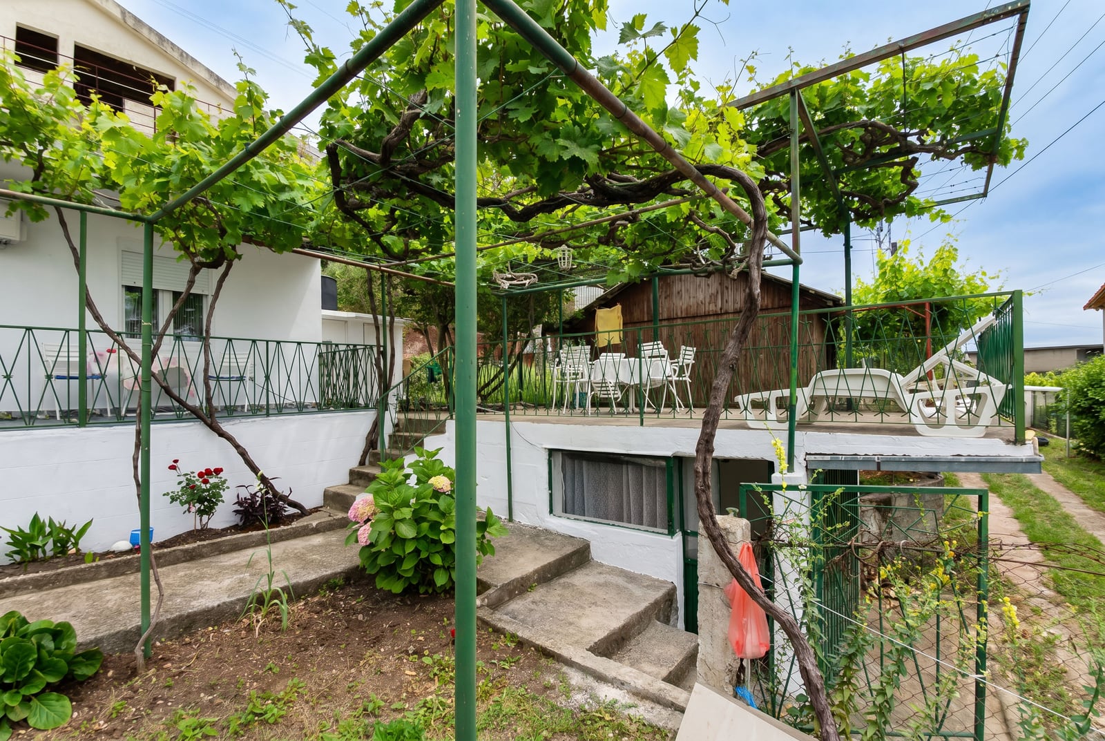 Cozy terrace of a house in Sutomore, Montenegro, featuring a grapevine pergola, garden furniture, and a lush green garden in the yard.