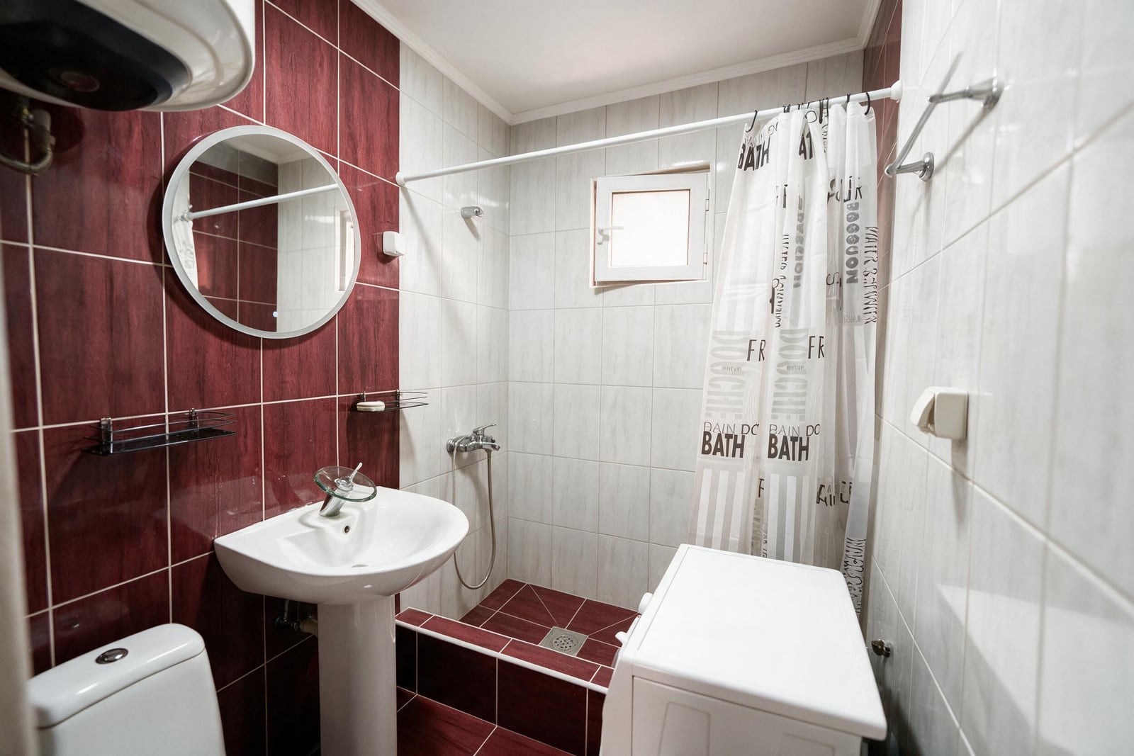 Bathroom featuring a pedestal sink, toilet, shower area with curtain, round mirror, and red tiled walls.