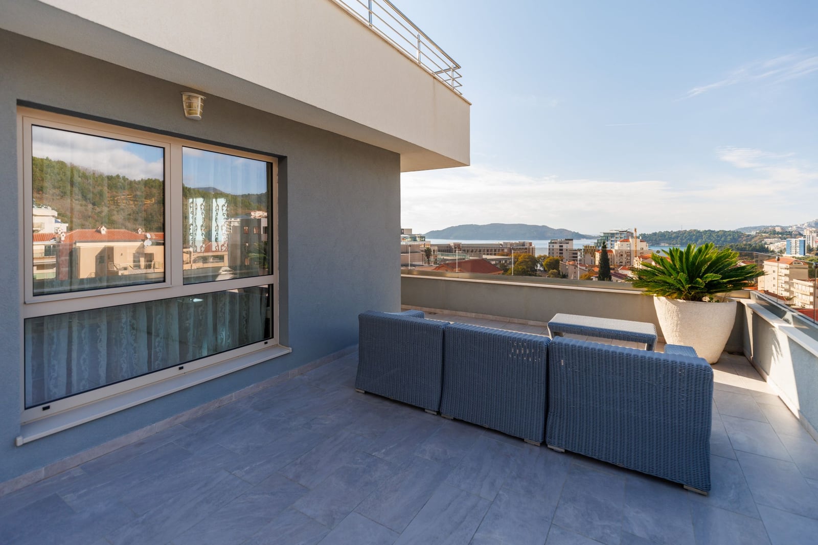 Spacious penthouse terrace in Becici, Montenegro, featuring wicker furniture and panoramic views of the sea and mountains.