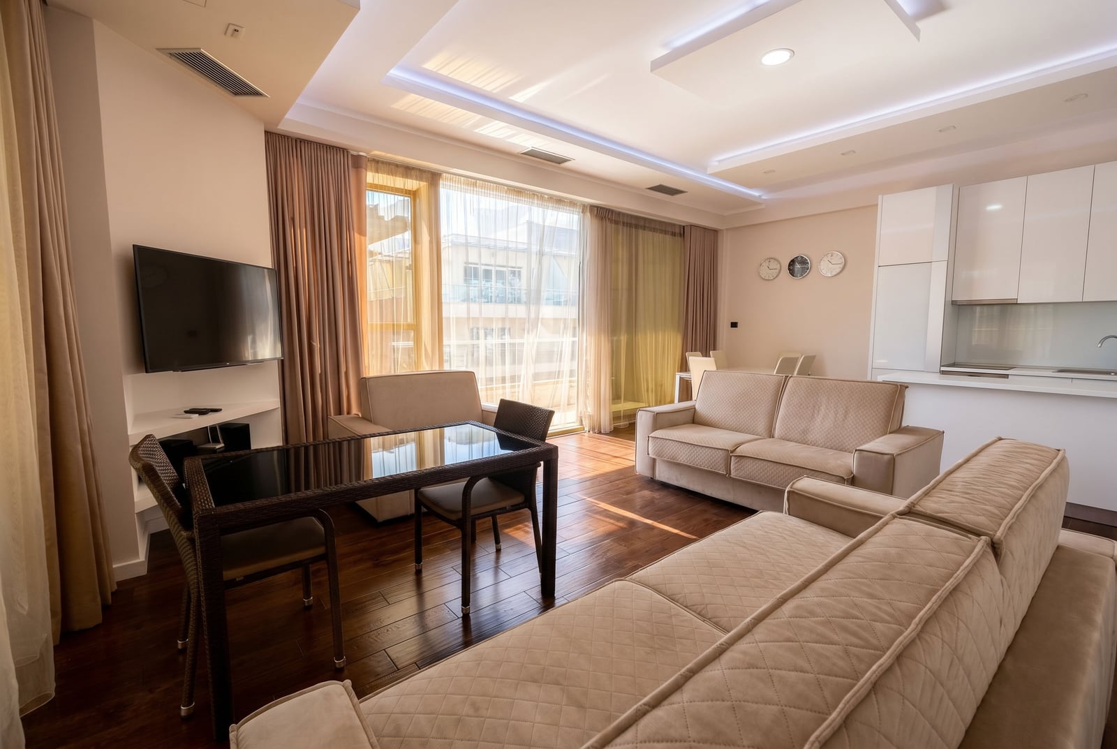 Modern living room with an open-plan kitchen in a Budva apartment, Montenegro: light-colored furniture, panoramic windows, and high-quality finishes.