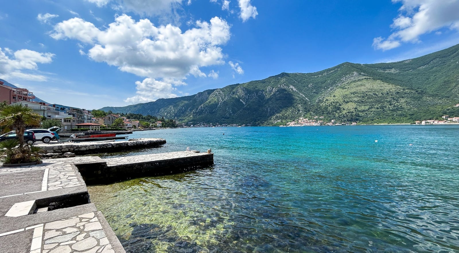 Sea and mountain view from a private villa pier in Dobrota, Montenegro. Clear water and coastline on a sunny day.