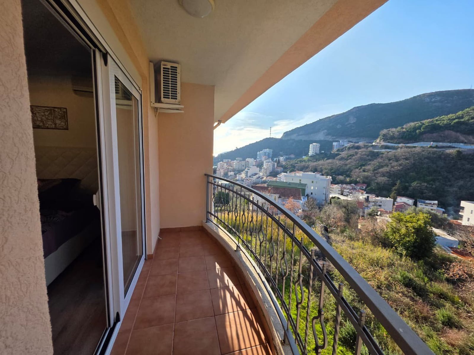 Balcony with panoramic views of the mountains and the city of Bečići, Montenegro, access from the bedroom, tiled flooring, wrought-iron railings.