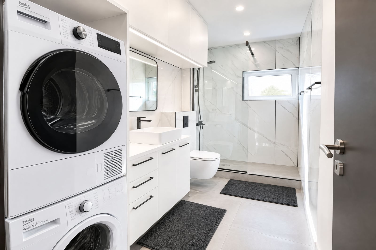 Modern bathroom featuring a stacked washer dryer, vessel sink vanity, wall-mounted toilet, and glass-enclosed shower area.