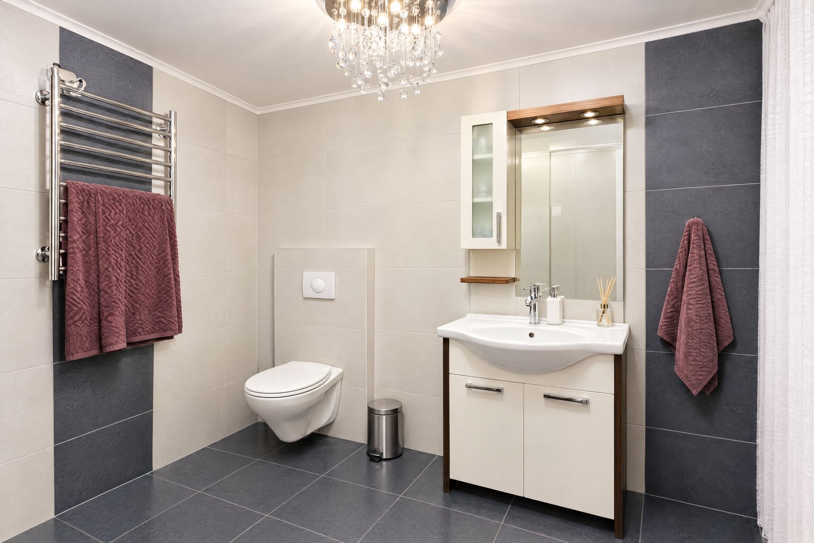 Modern bathroom featuring a wall-mounted toilet, vanity sink, heated towel rail, and crystal chandelier.