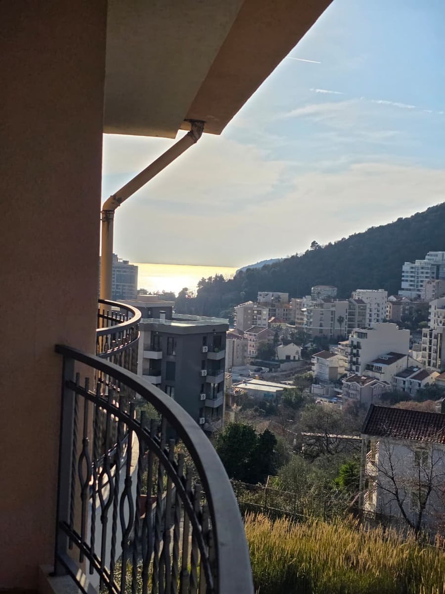 View from the apartment balcony in Bečići, Montenegro: a panorama of the city, mountains, and coastline on a sunny day.