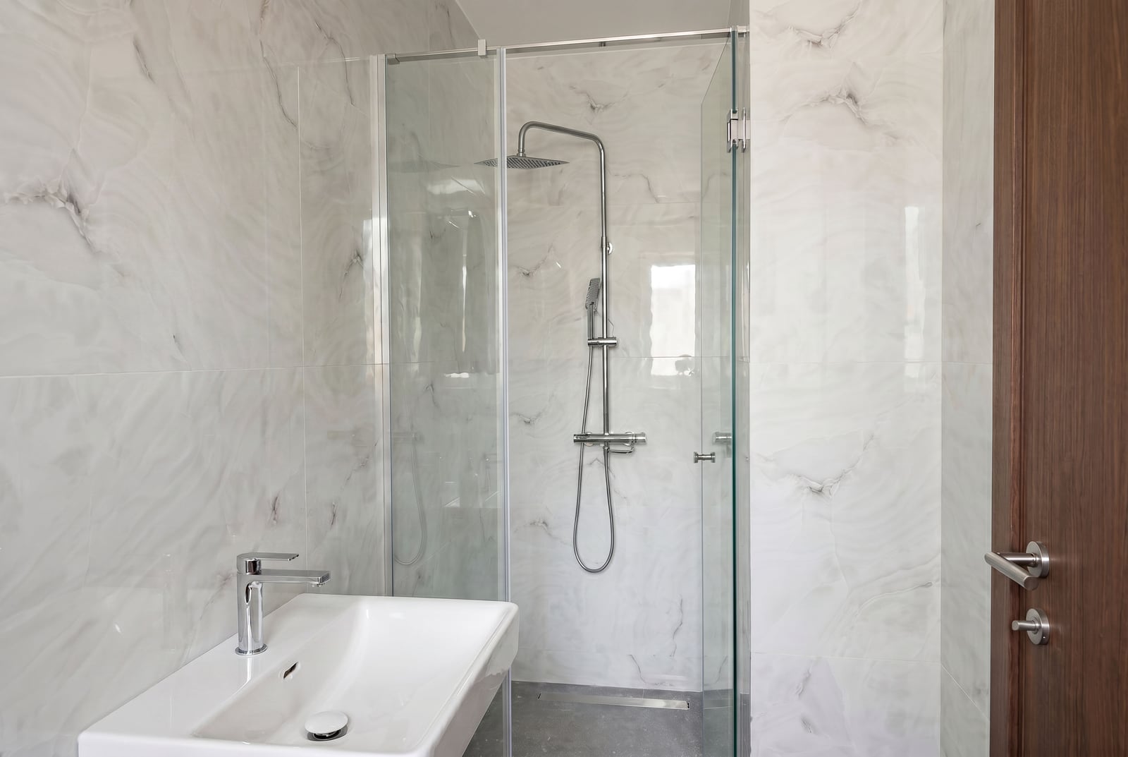 Modern bathroom in an apartment in Budva, Montenegro: shower cabin, light marble-look tiles, and sanitary ware.