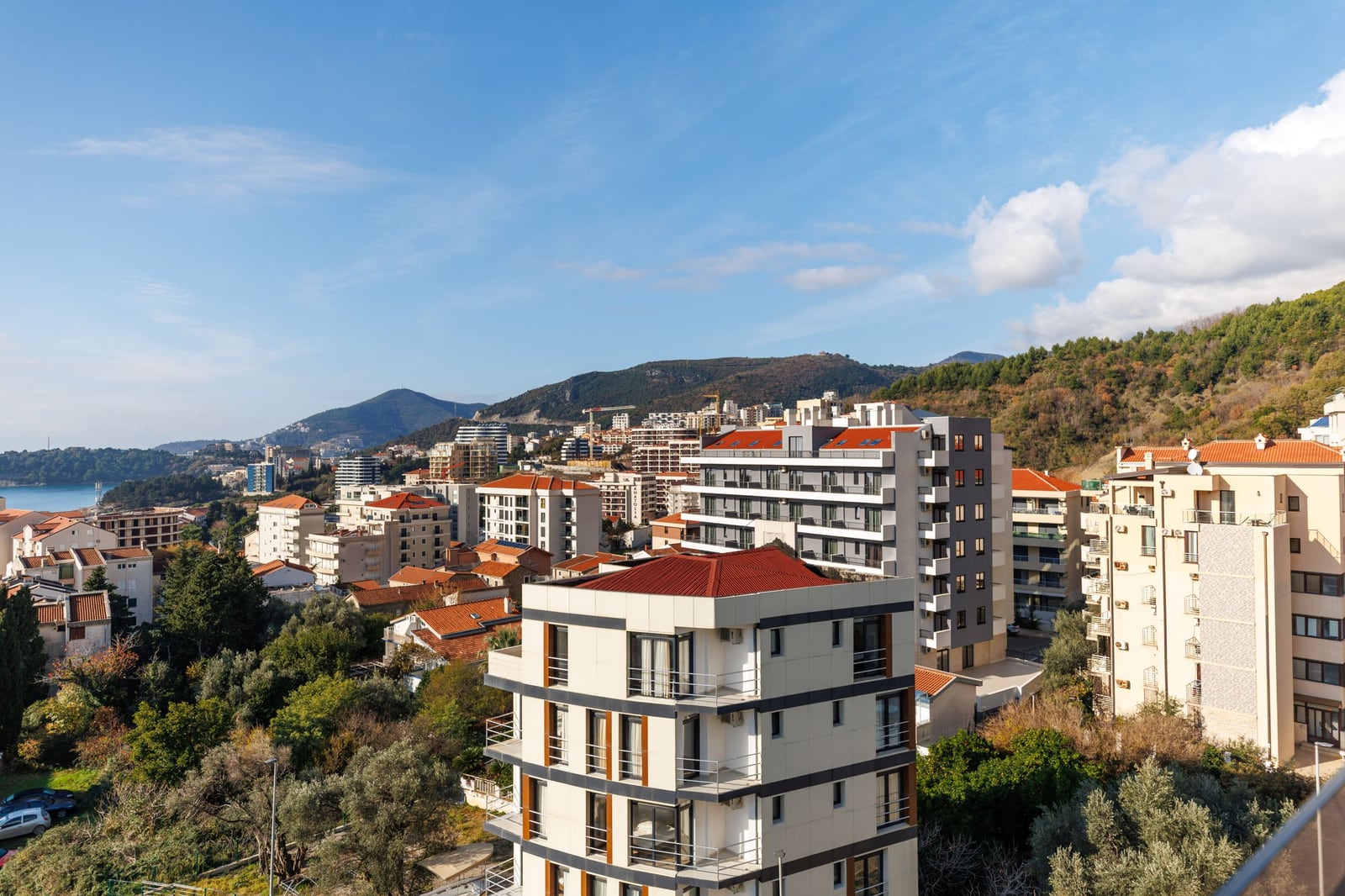 Panoramic view of a residential complex and mountains in Bečići, Montenegro: modern houses with red roofs and a seascape.