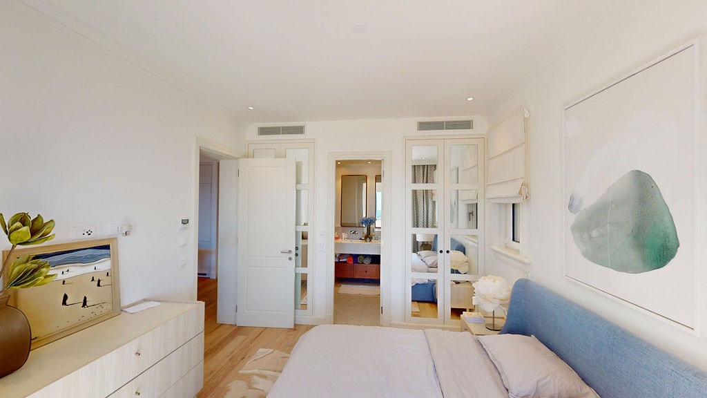 Bright bedroom with a blue bed and mirrored wardrobe in an apartment in Luštica, Montenegro. View of the bathroom.