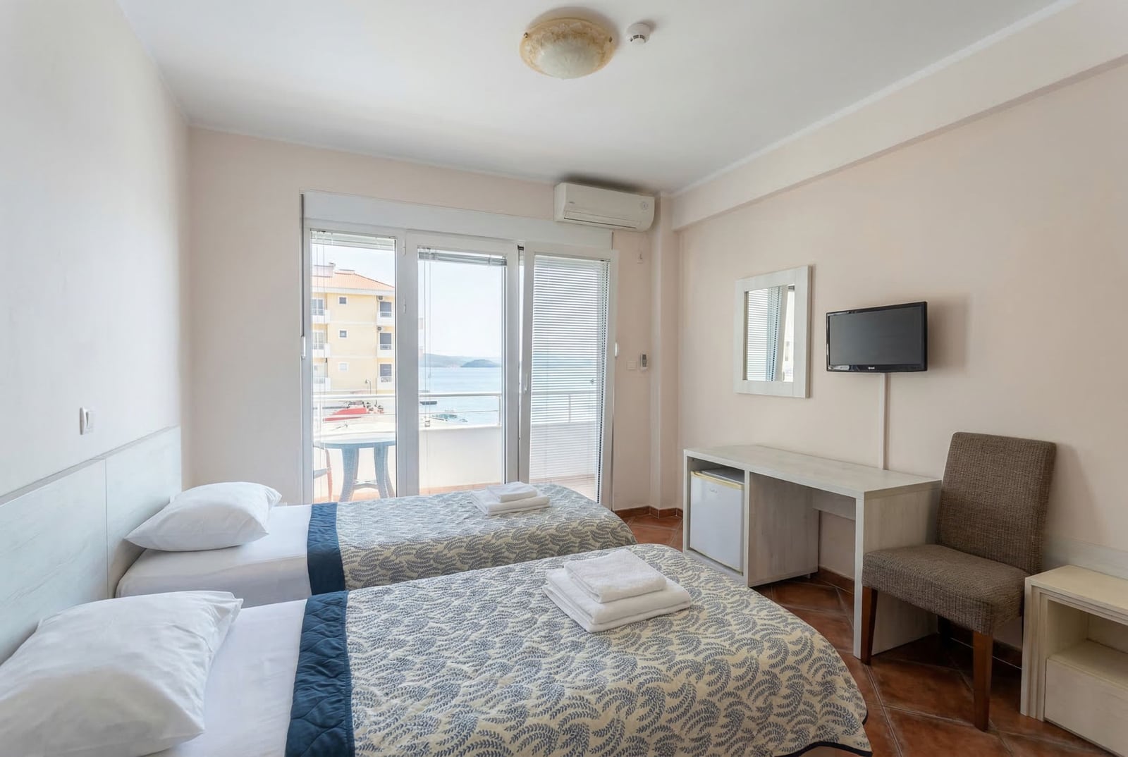 Hotel bedroom in Bečići, Montenegro: two beds, a desk, TV, and access to a balcony with sea view.