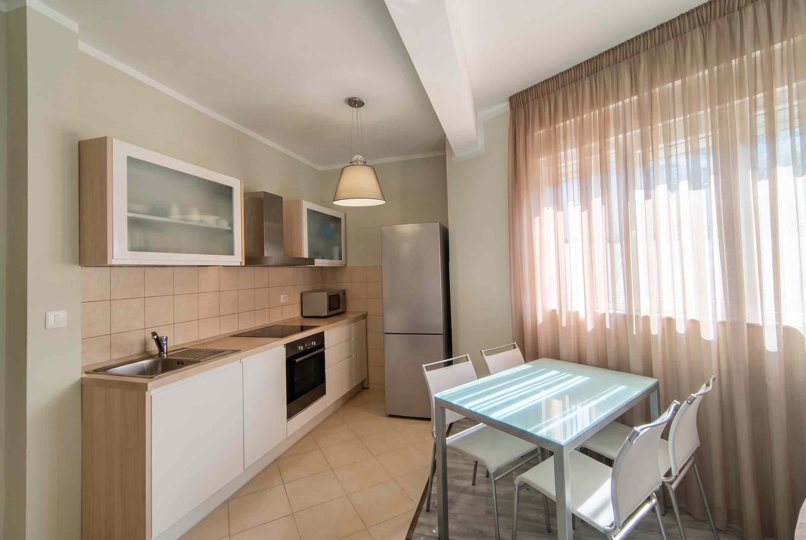 Modern kitchen with light-colored cabinetry and a dining area in an apartment, Bečići, Montenegro.
