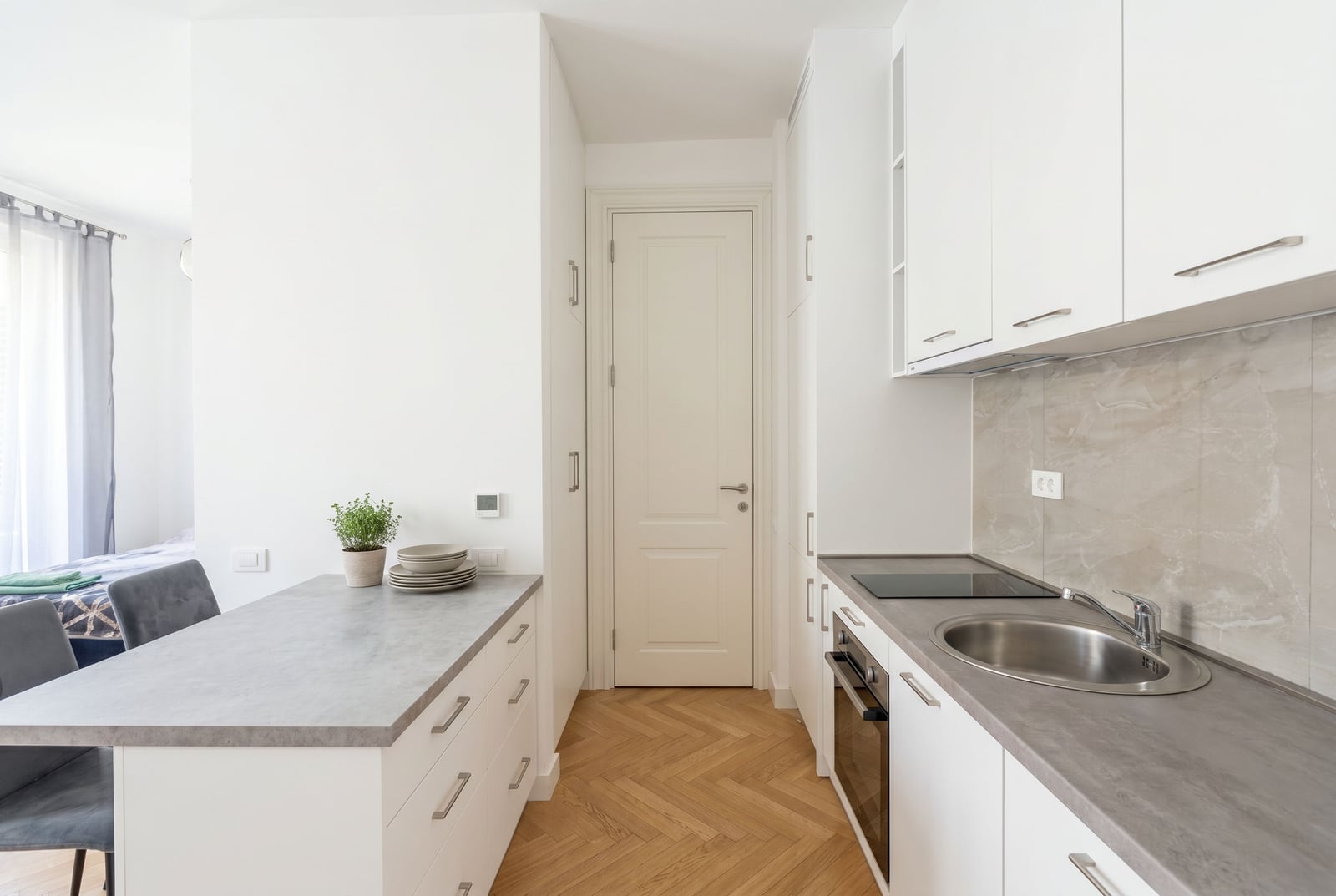 Modern white kitchen with an island and parquet flooring in an apartment in Bečići, Montenegro. Cozy interior with new appliances.