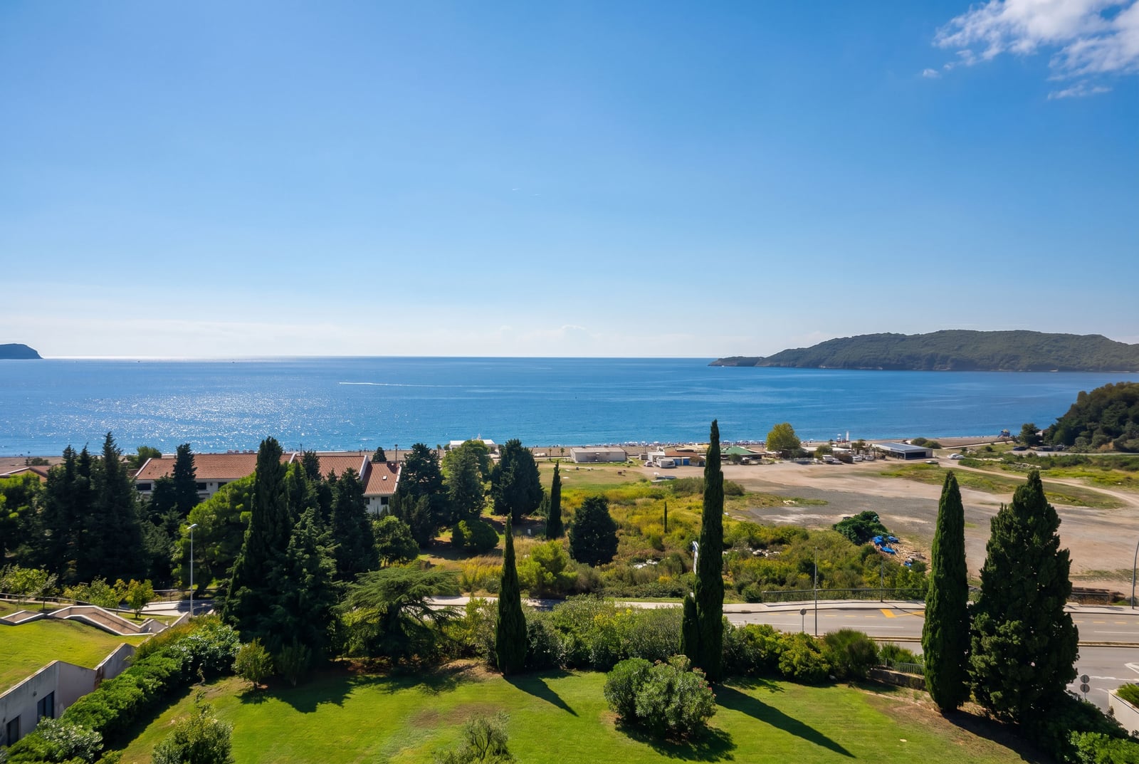 Panoramic view of the sea and Becici beach, Montenegro: green garden, cypress trees, and the coastline as seen from an apartment window.