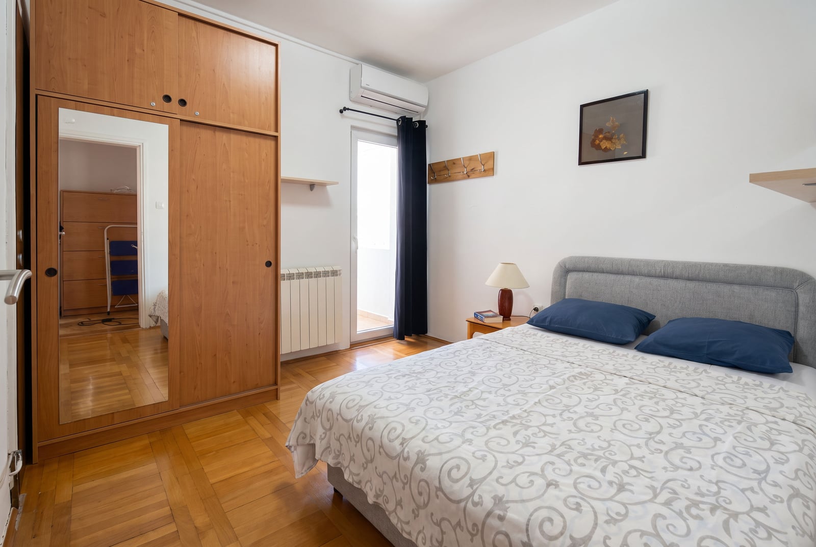 Bedroom featuring a double bed with blue pillows, a large wooden wardrobe with a mirror, and an AC unit.