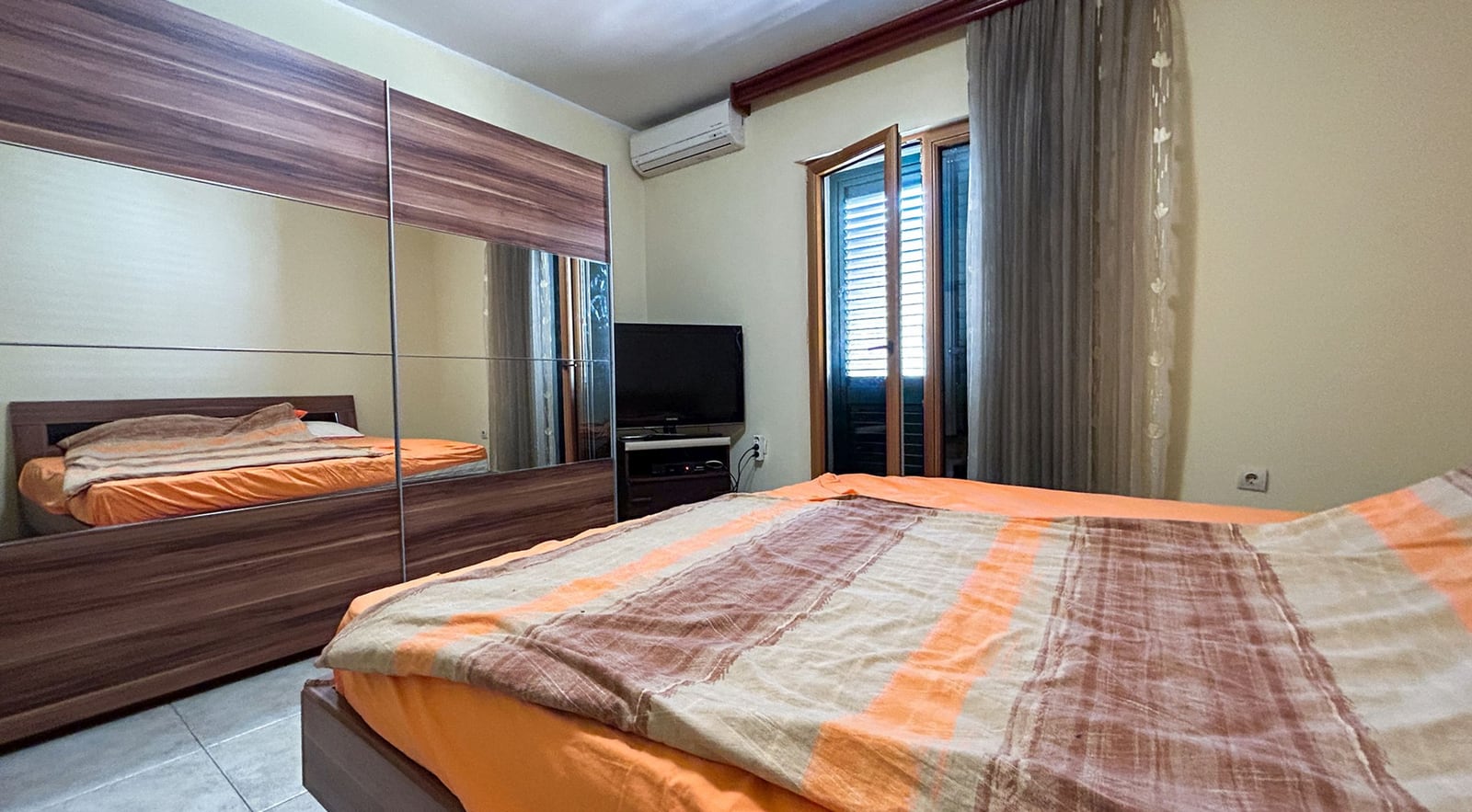 Bedroom in a villa in Dobrota, Montenegro: double bed, mirrored sliding wardrobe, TV, and access to the balcony.