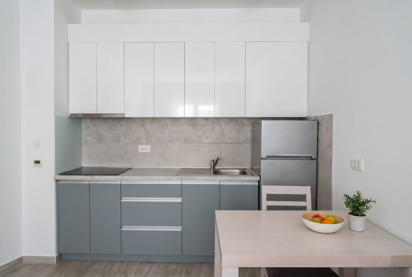 Modern kitchen in an apartment in Budva, Montenegro: white and gray cabinetry, built-in appliances, and a dining area.