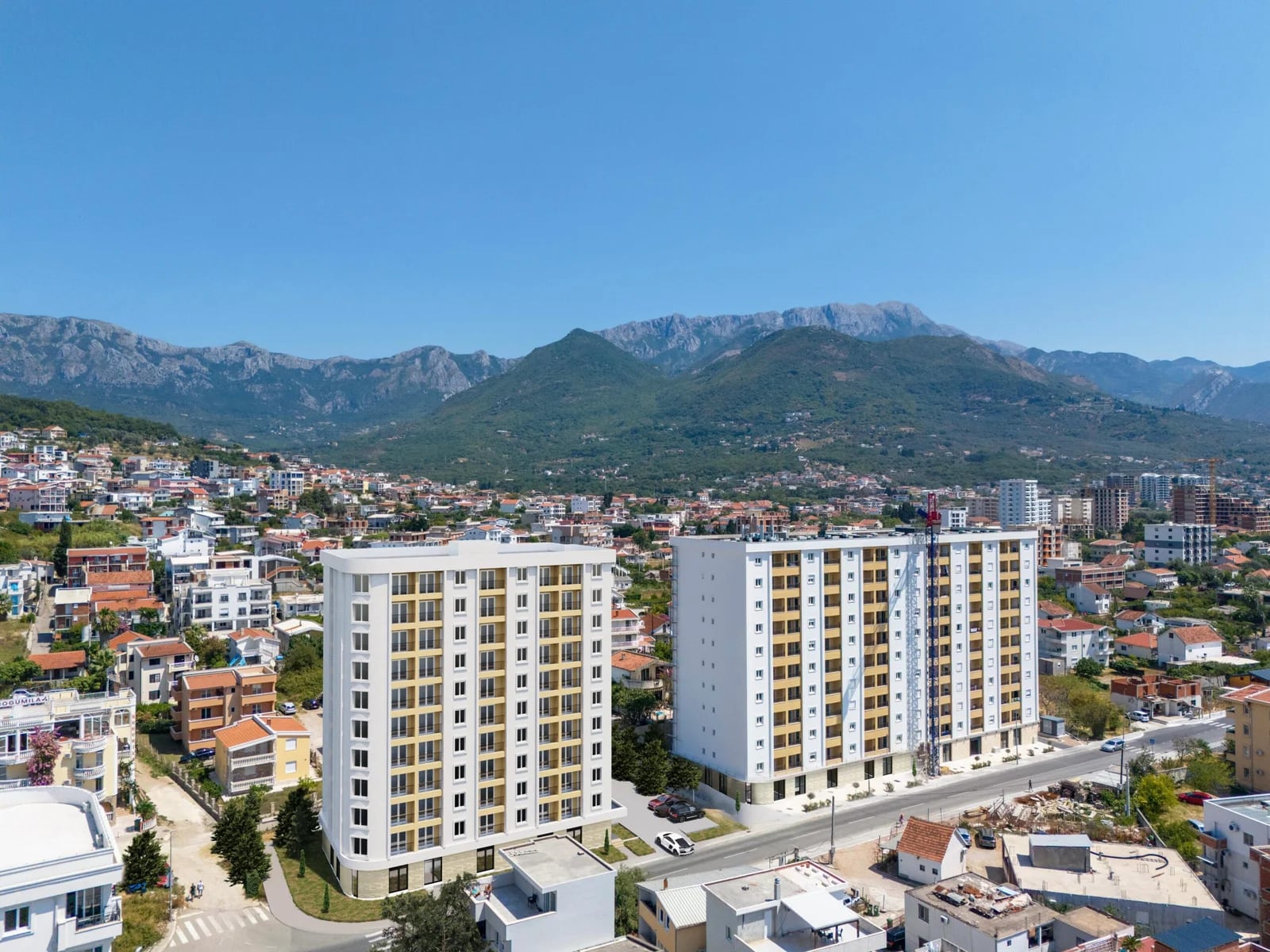 Aerial view of modern residential complexes in the city of Bar, Montenegro, against a backdrop of scenic mountain landscapes.