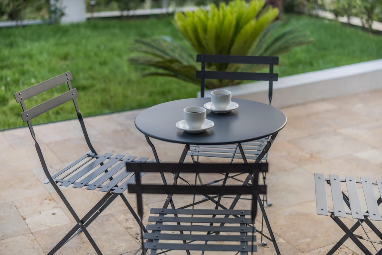 Cozy terrace with a coffee table at a villa in Budva, Montenegro, overlooking a green garden and a palm tree.