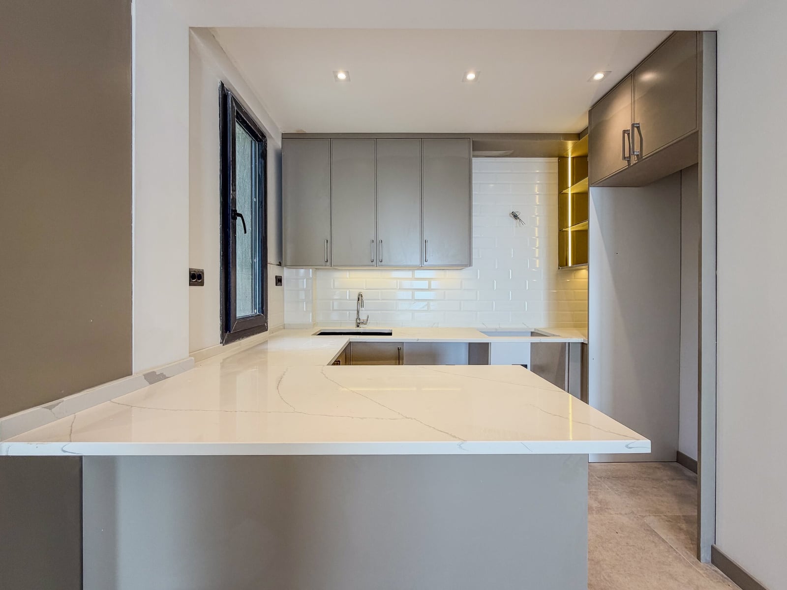 Modern kitchen featuring a white marble island, grey cabinetry, subway tile backsplash, and under-cabinet lighting.