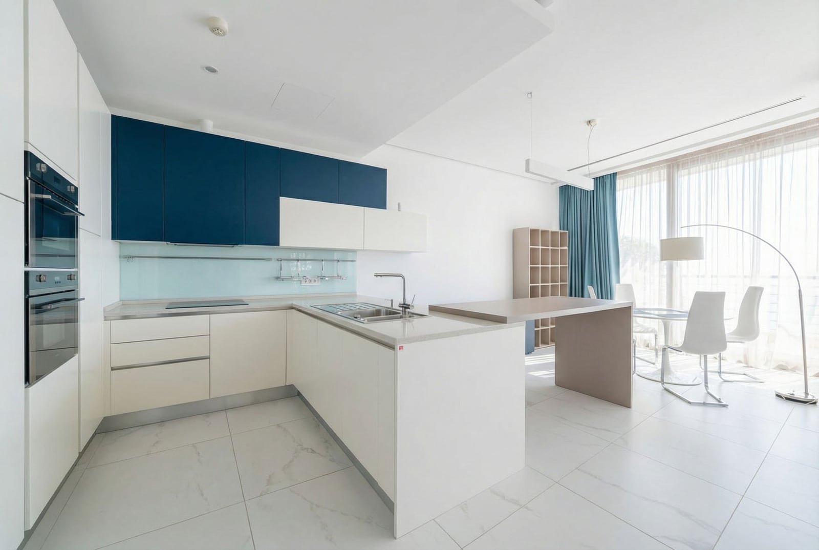 Modern kitchen-living room in Dukley, Budva, Montenegro: white furniture, an island, and panoramic windows with a view.