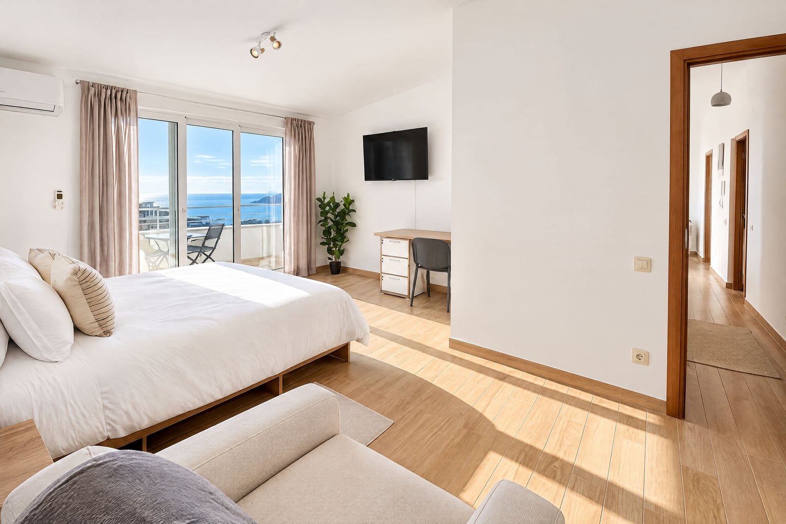 Bright bedroom with a double bed, desk, and sliding glass doors leading to a balcony with sea views.