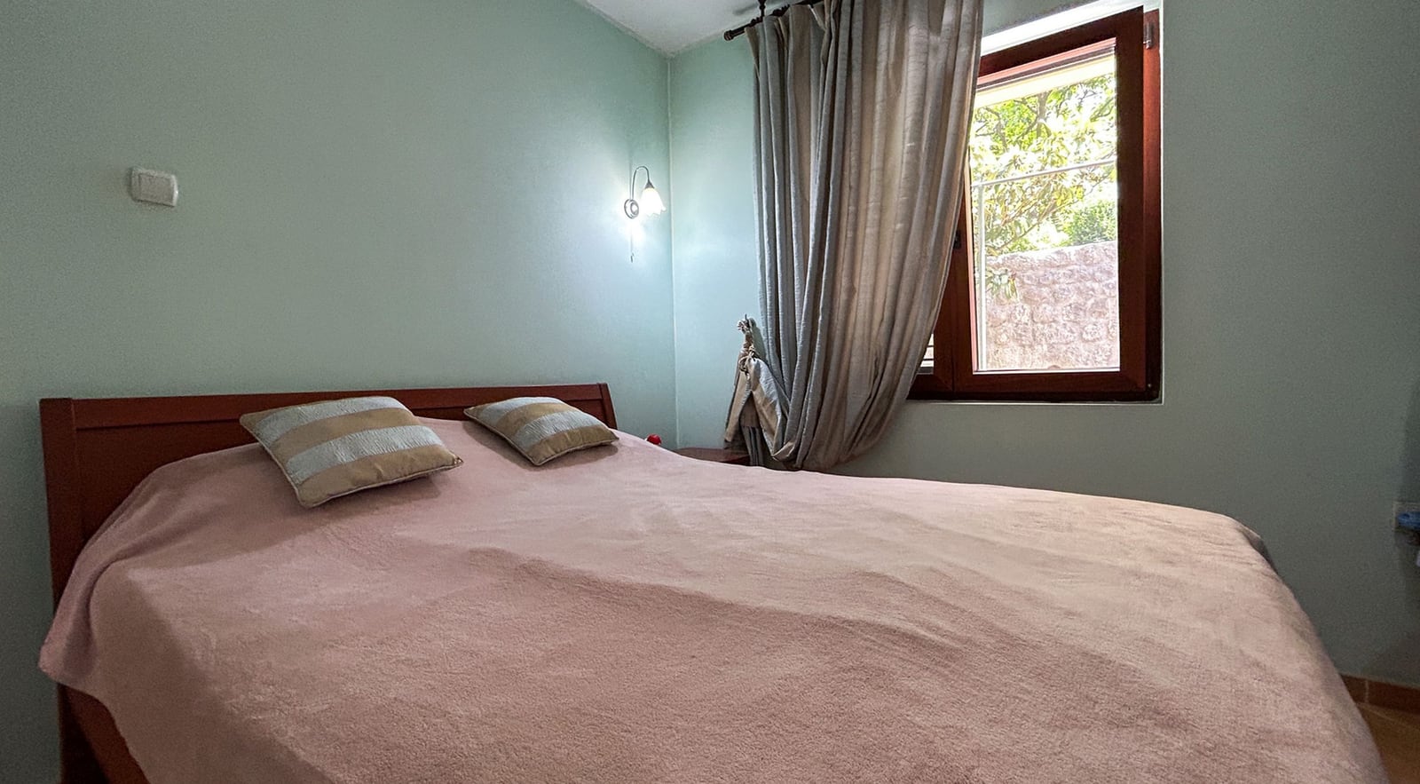 Cozy bedroom with a double bed in a villa in Dobrota, Montenegro: light walls, wooden furniture, and a view from the window.