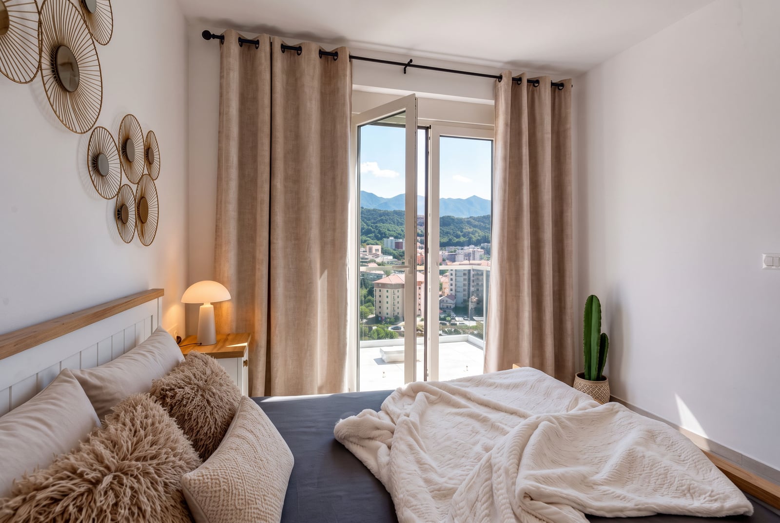 Bright bedroom featuring a double bed, beige curtains, wall mirror art, and a city view through glass doors.