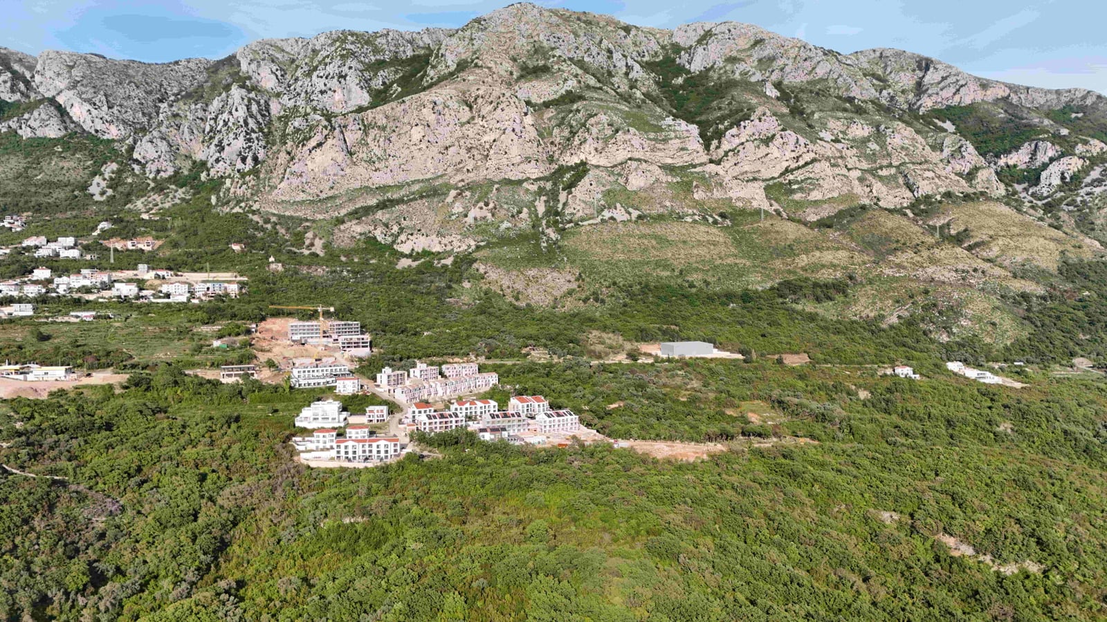 Aerial view of a land plot and residential complex in Markovići, Montenegro, against a mountain landscape backdrop.