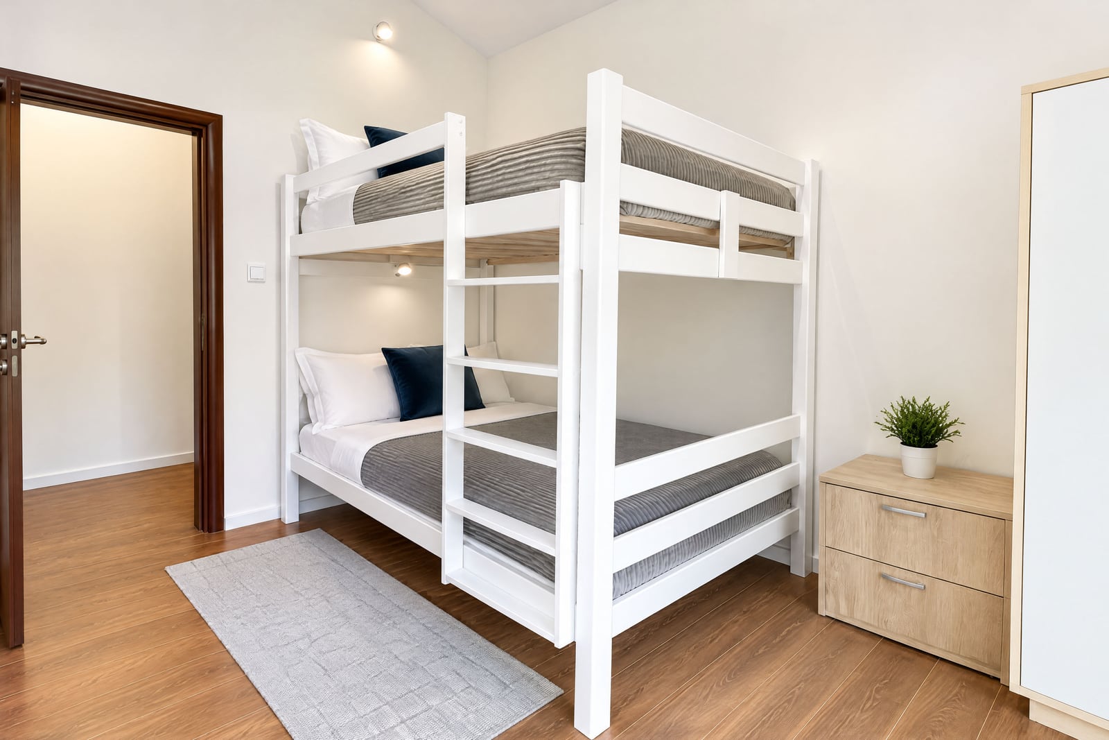Bright bedroom featuring a white bunk bed, wooden flooring, and light walls with a small rug.