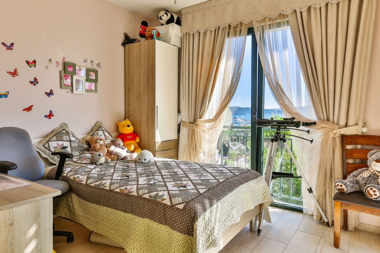 Children's bedroom with a bed and sea view in a villa, Tivat, Montenegro. Light-colored furniture, panoramic window, and balcony.