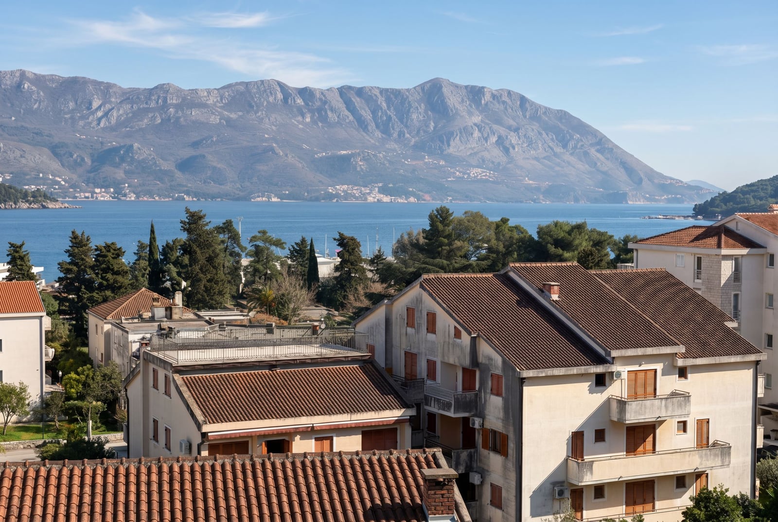 Panoramic sea and mountain view from an apartment in Budva, Montenegro: a residential area with tiled roofs and greenery.