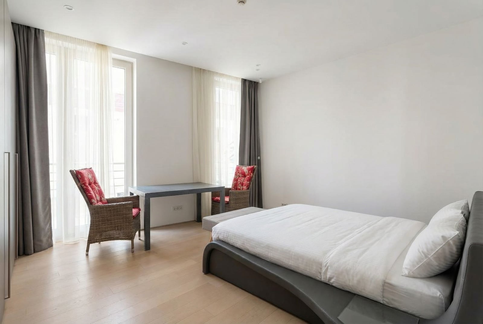 Bright bedroom in Dukley apartments, Budva, Montenegro: a double bed, wicker chairs, and panoramic windows.