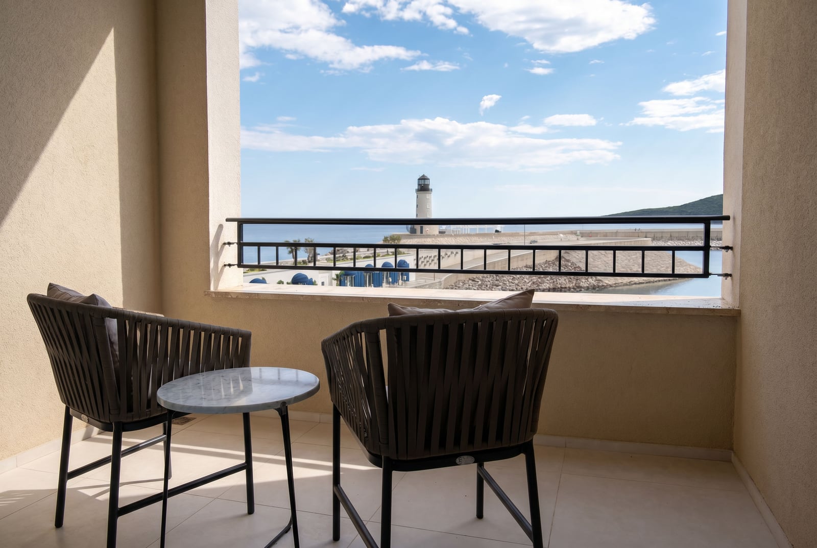 Balcony with wicker furniture and a view of the lighthouse and the sea in Luštica Bay, Montenegro. Modern apartment interior.