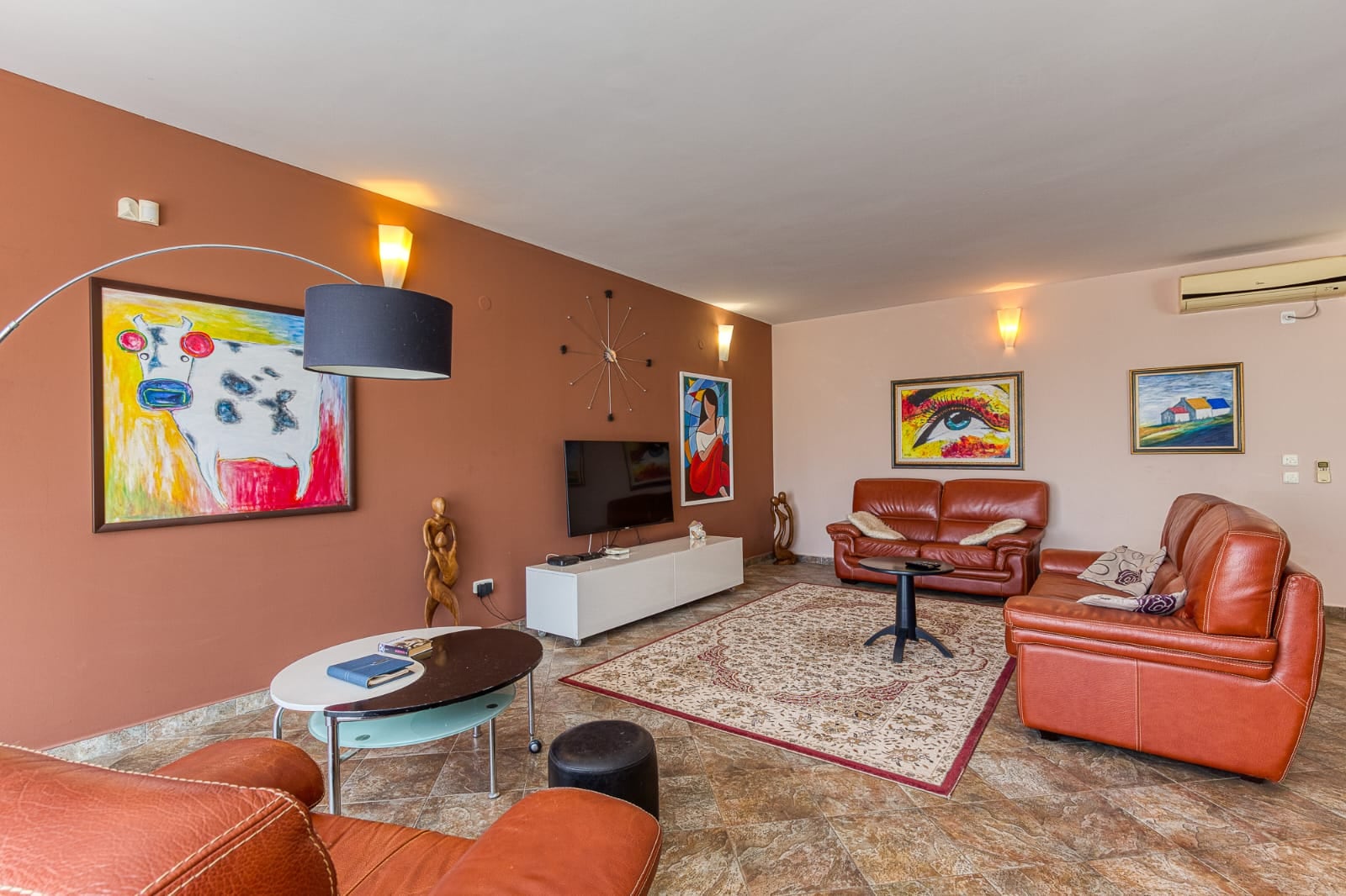 Living room with leather furniture and paintings in a villa in Becici, Montenegro. Cozy interior with a TV and a light-colored rug.