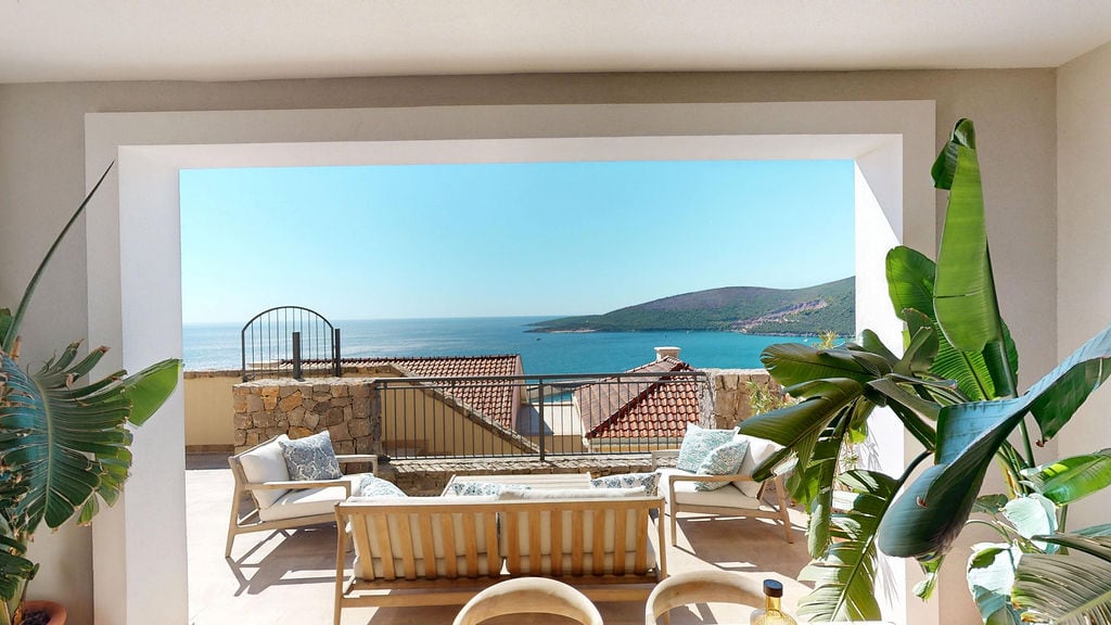 Terrace with sea view in the Luštica residential complex, Montenegro: wicker furniture, tropical plants, and a panoramic view of the bay.