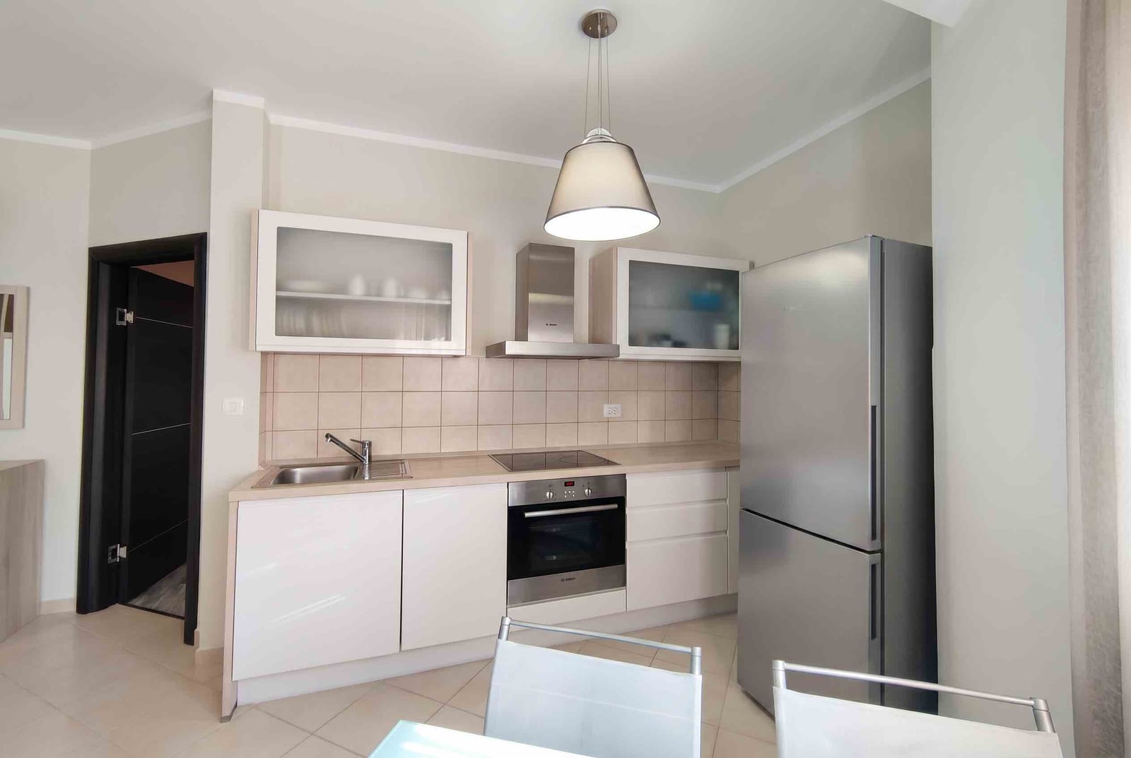 Modern bright kitchen in an apartment in Bečići, Montenegro: white cabinets, built-in appliances, and a dining area.