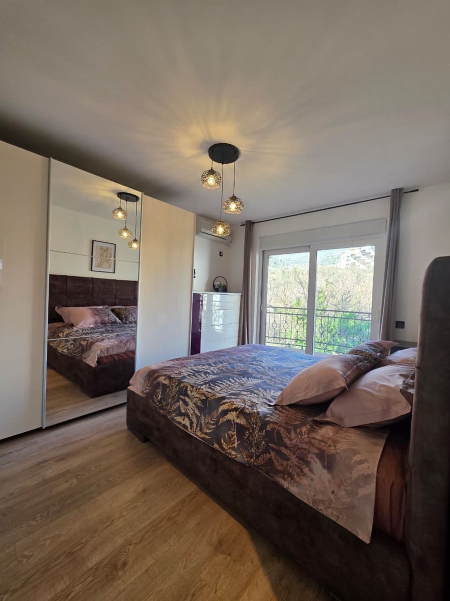 Modern bedroom with a double bed, mirrored wardrobe, and access to the balcony in an apartment, Becici, Montenegro.