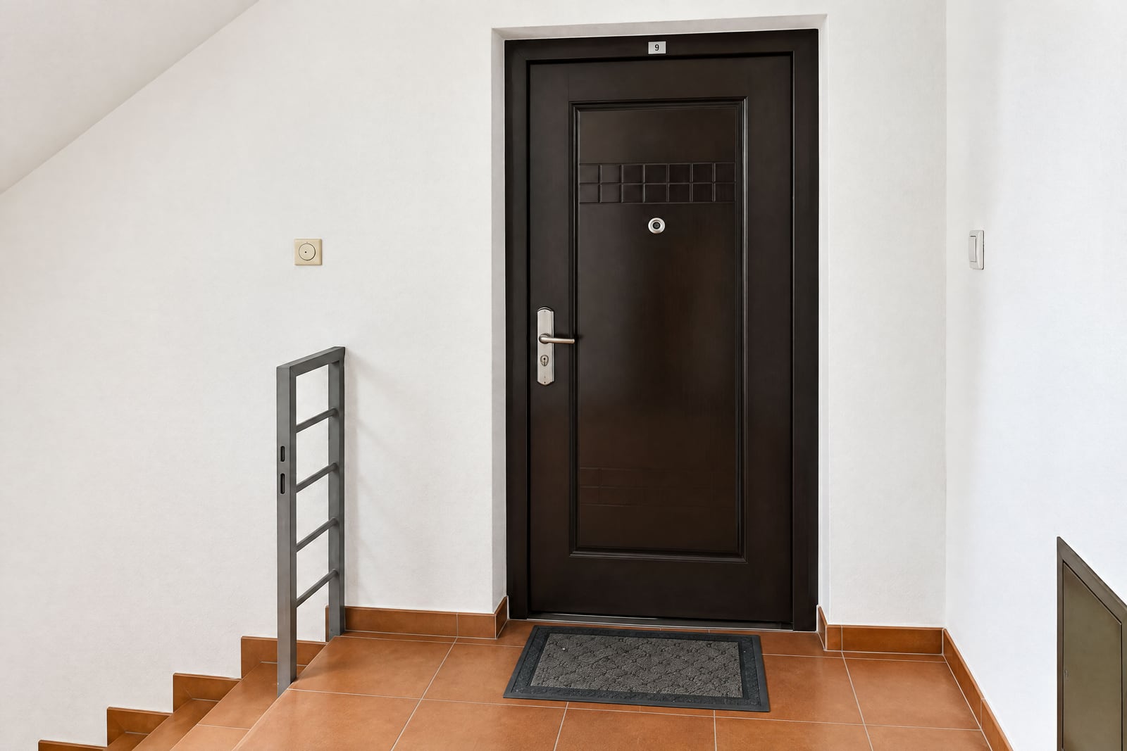 Apartment entrance door number 9 in a hallway with stairs and terracotta floor tiles.