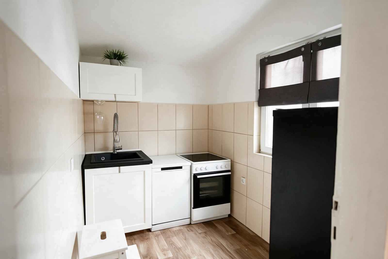 Small kitchen featuring white cabinets, a black sink, stove, dishwasher, and refrigerator against beige tiles.