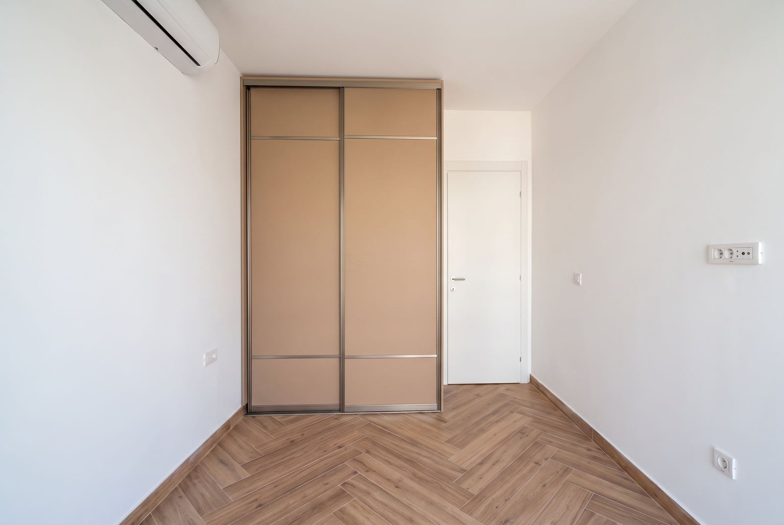 Bedroom in an apartment in Tivat, Montenegro: built-in wardrobe, light wall finishes, and herringbone-pattern flooring.