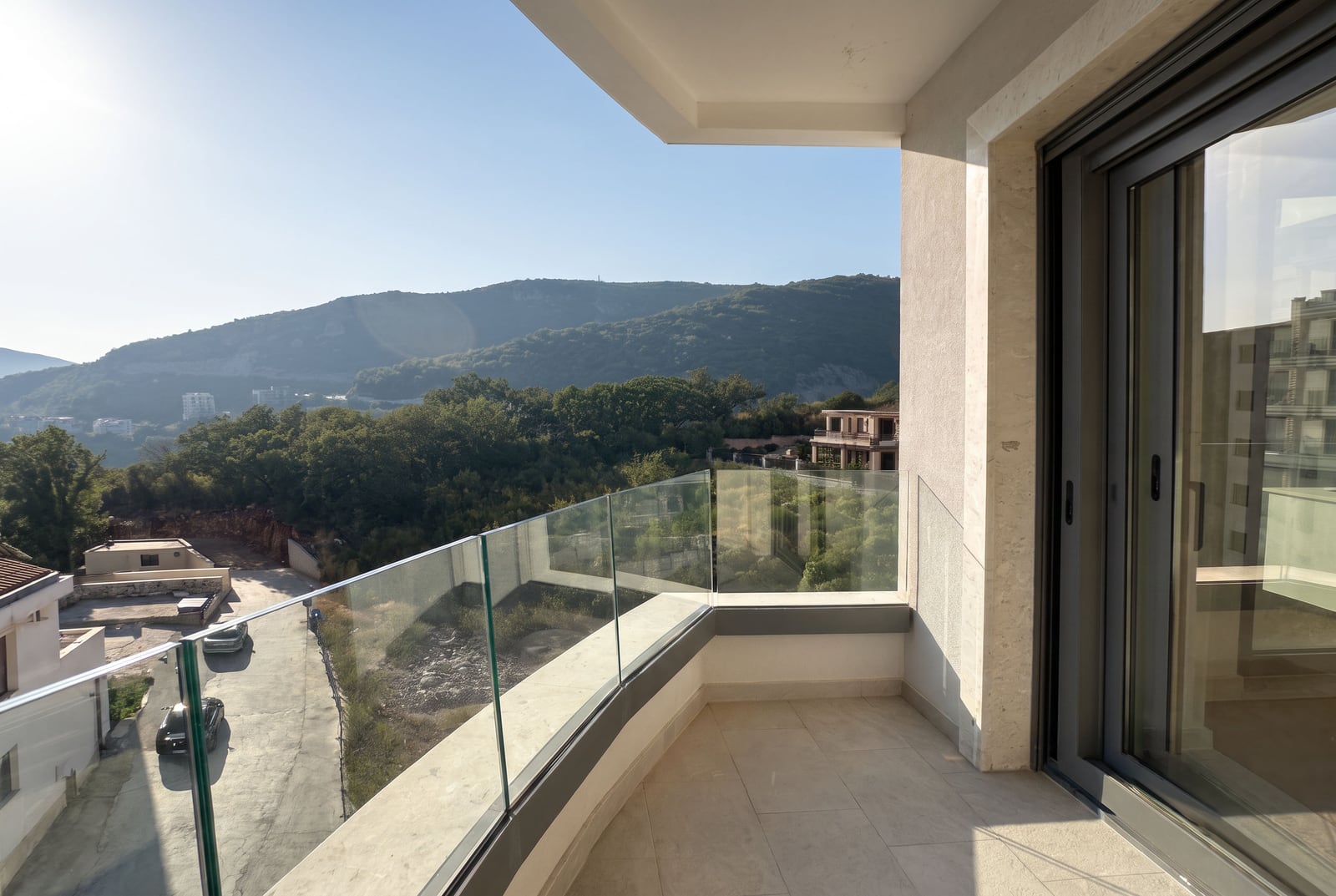 Modern balcony with glass railing overlooking hills and trees under a clear sky.