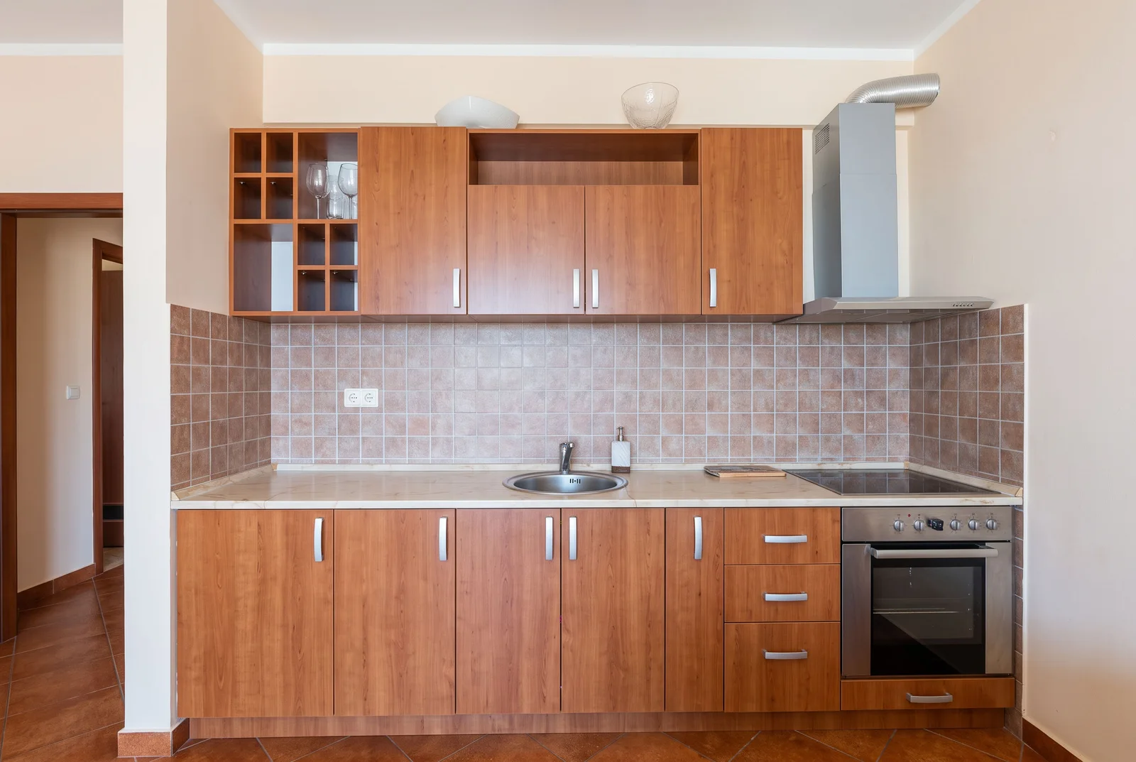 Kitchen with wooden cabinets, sink, cooktop, oven, and range hood against a tiled backsplash.