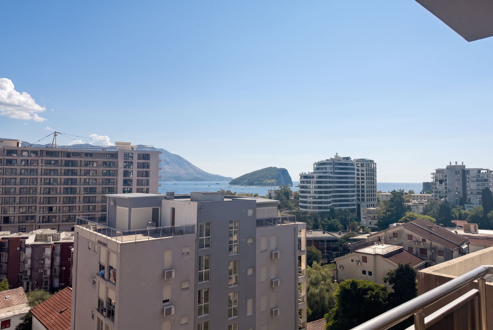View from a balcony showing city buildings, the sea, and a mountain peninsula under a clear blue sky.
