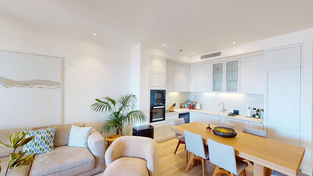 Modern living room with a white kitchen and dining area in an apartment at the Luštica residential complex, Montenegro. Bright interior with furniture.