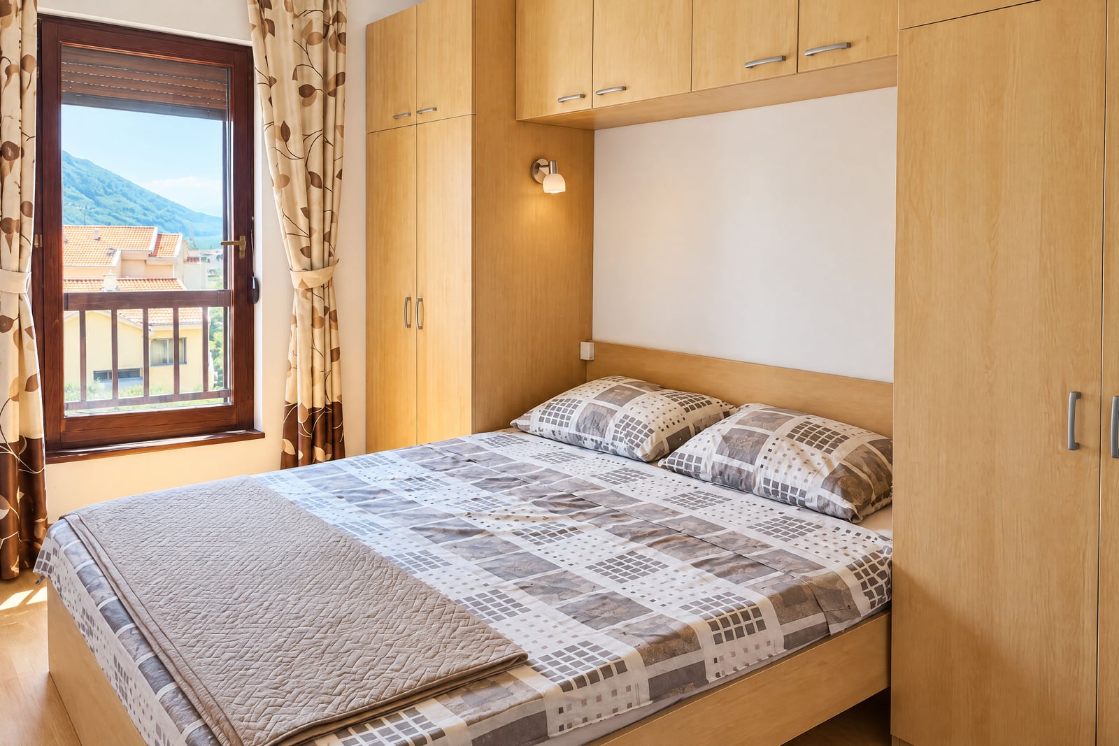 Bedroom featuring a wooden bed, built-in wardrobe, and window overlooking mountains and rooftops.