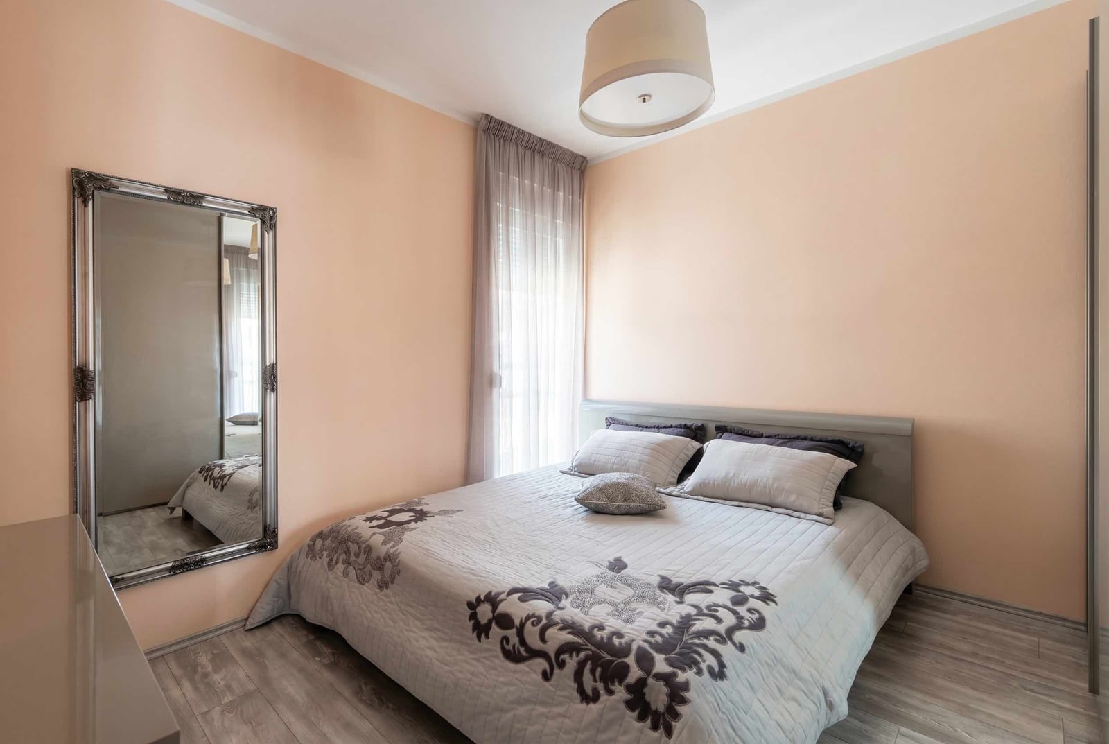 Cozy bedroom with a double bed and a mirror in an apartment, Bečići, Montenegro. Bright interior with laminate flooring.