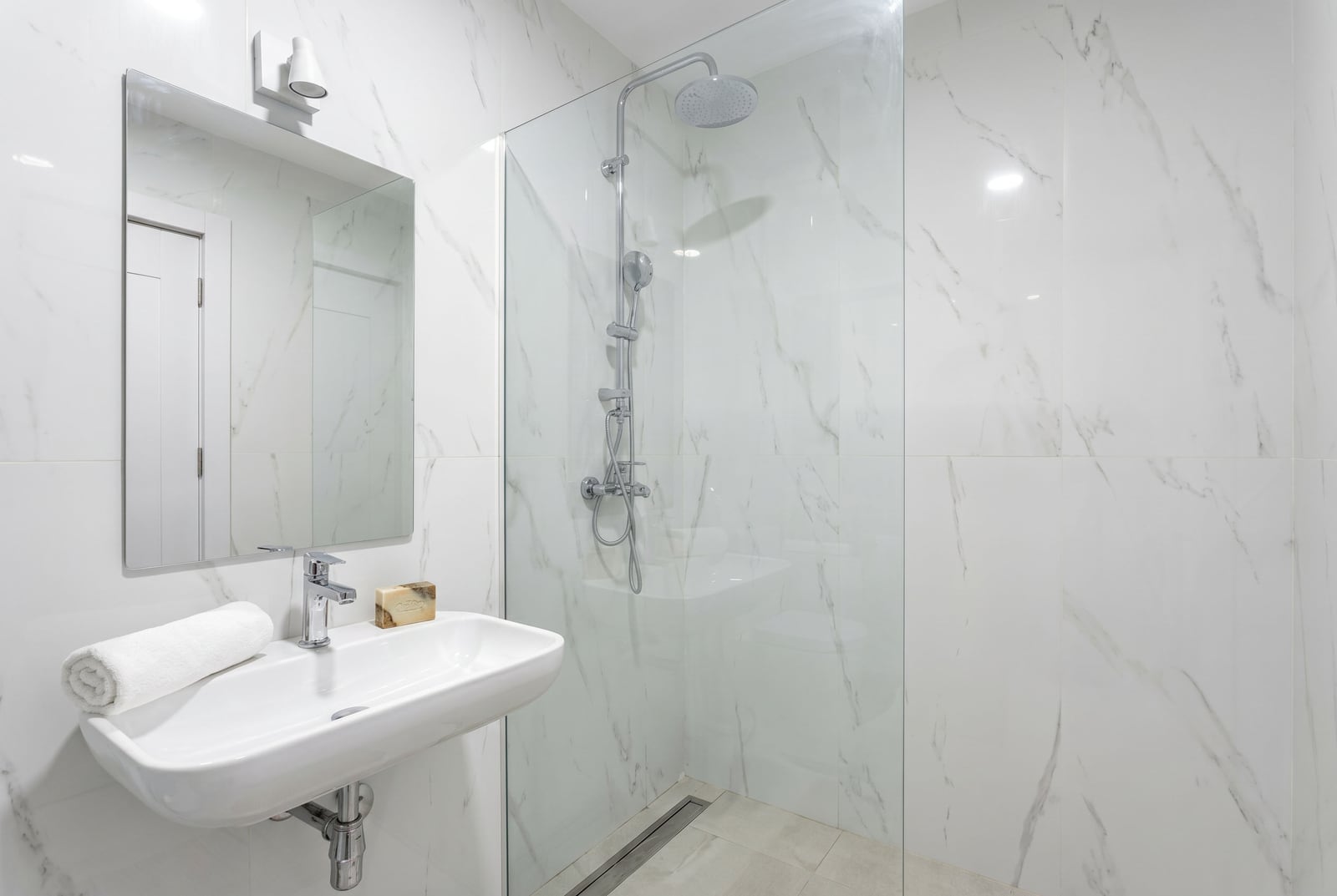 Modern bathroom in an apartment in Bečići, Montenegro: walk-in shower, white marble-effect tiles, and stylish fixtures.